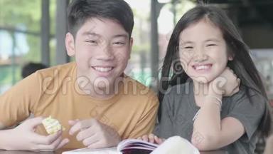 亚洲男孩和女孩用<strong>卡通书</strong>放松，可爱的亚洲孩子坐在咖啡馆里享受读书，微笑着面对
